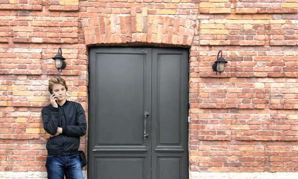 一个年轻人站在砖房的前门附近图片下载