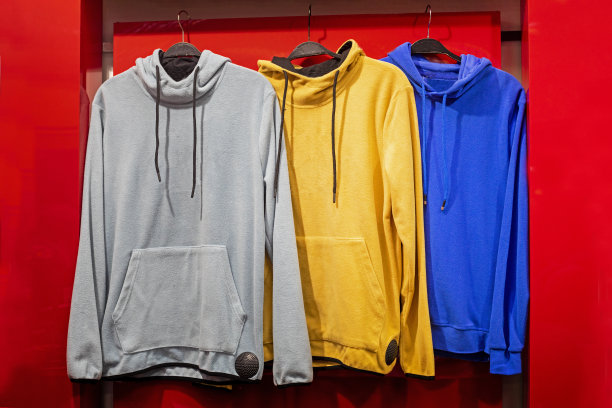 时髦的灰黄蓝连帽衫挂在红色背景的衣架上。生活方式图片下载