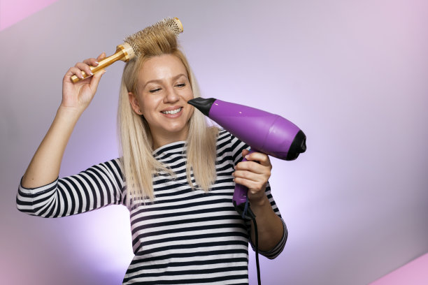 有魅力的年轻女子带着吹风机和梳子微笑，工作室拍摄图片下载