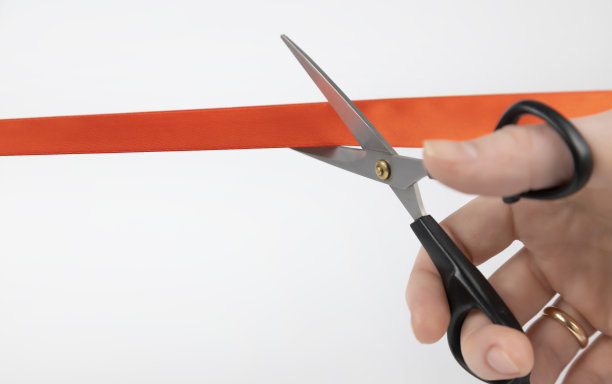剪红丝带。一个女人的手用剪刀剪红丝带的特写图片下载