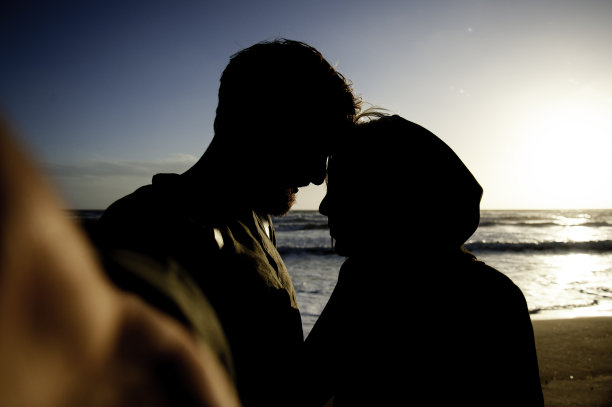 热恋的情侣在日落时分的荒芜海滩上自拍——女友和她的潮人男友在背光下自拍时相视相视，玩得很开心图片下载