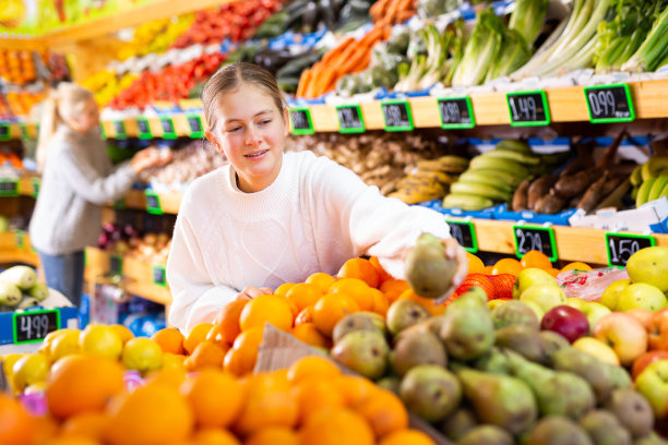 快乐的少女在超市挑选成熟的水果图片下载