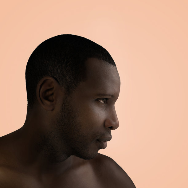 一个英俊的男子与黑皮肤的艺术肖像，侧面视图，浅鲑鱼背景，照片图片下载