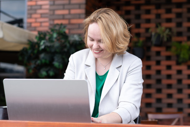 快乐的微笑女人使用应用程序在一个街头咖啡馆的数字笔记本电脑。图片下载