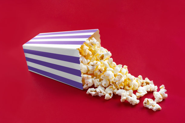 美味的奶酪爆米花从紫色条纹的纸盒桶里掉出来，孤立在红色的背景上图片下载
