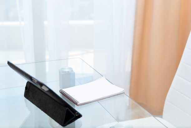 数码平板电脑和笔记本放在玻璃桌上，白色的空椅子为在家学习准备。远程学习在线教育理念。有选择性的重点图片下载