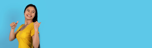 开朗漂亮的年轻韩国女性在黄色t恤指向自由的空间在后面图片下载