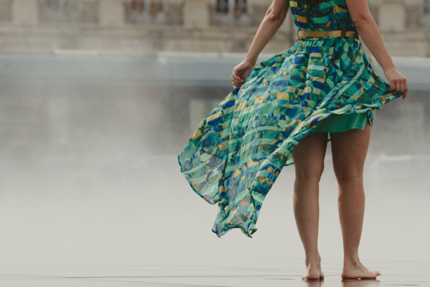 一个穿着夏装的年轻女子赤脚走过潮湿的广场。图片下载