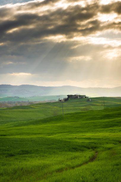 在意大利托斯卡纳乡村的绿色田野上，令人惊叹的光束穿过云层图片下载