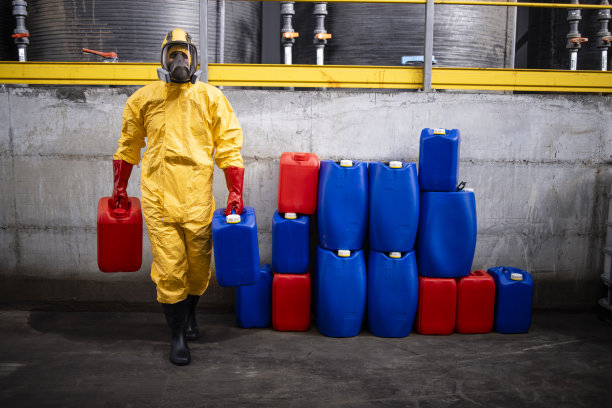 穿着防护服和防毒面具的化工工人在工厂搬运危险物品。图片下载