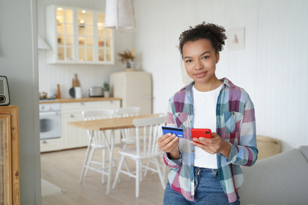快乐的非裔美国女孩正在用手机和信用卡从家里网购。图片下载