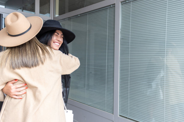 两个朋友在一幢大楼的入口处互相拥抱问候图片下载