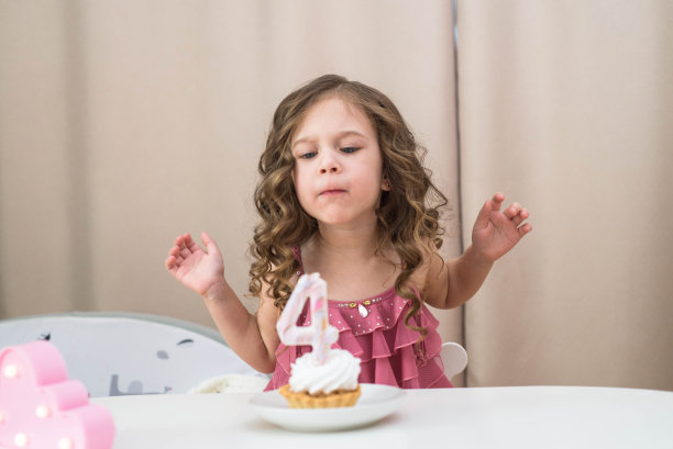 小女孩在灯光室的白色桌子上对着生日蛋糕吹蜡烛。图片下载