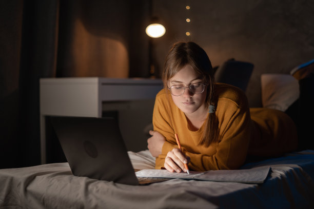 女生晚上在宿舍用笔记本电脑在床上学习。图片下载