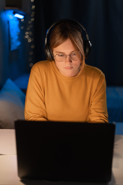 年轻聪明的女学生穿着毛衣工作在她的笔记本电脑在大学宿舍深夜。图片下载