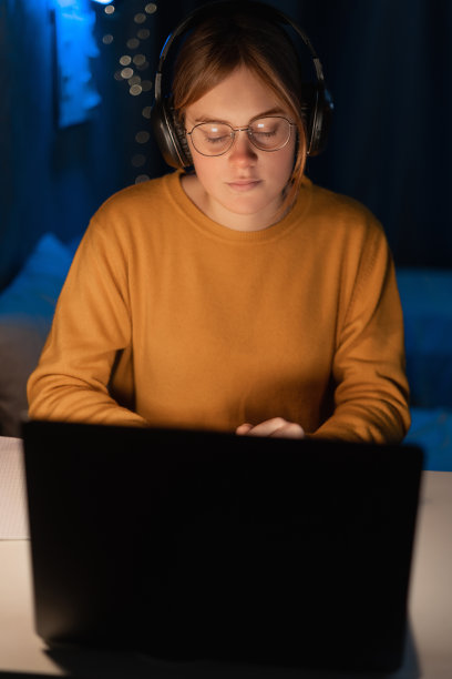 年轻学生戴着耳机在大学校园或宿舍使用笔记本电脑。女大学生远程学习。图片下载