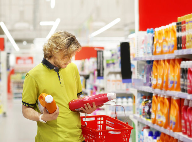 男子在超市购物，阅读产品信息(尿布，洗涤剂)。图片下载