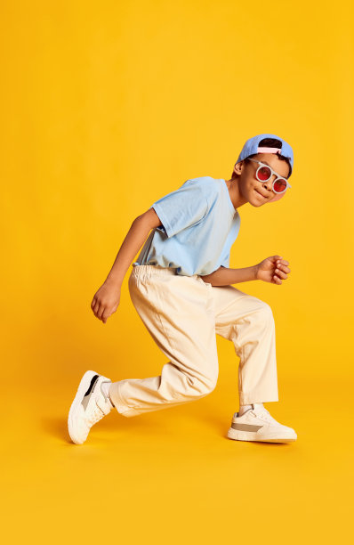 动态的肖像小非洲男孩，嘻哈舞者在时尚街头风格的衣服跳舞在明亮的黄色背景。观念音乐，舞蹈幸福图片下载