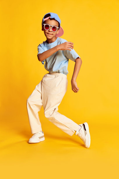 动态的肖像小非洲男孩，嘻哈舞者在时尚街头风格的衣服跳舞在明亮的黄色背景。观念音乐，舞蹈幸福图片下载