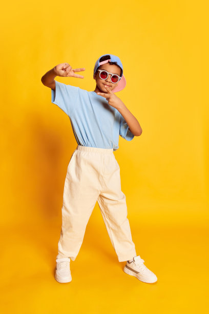 动态的肖像小非洲男孩，嘻哈舞者在时尚街头风格的衣服跳舞在明亮的黄色背景。观念音乐，舞蹈幸福图片下载
