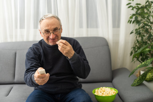 一位老先生坐在沙发上看电视。图片下载
