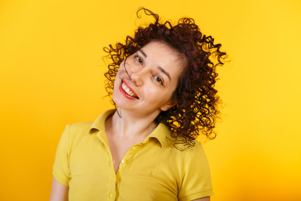 工作室拍摄的积极和微笑的女孩摇着头。穿着亮黄色t恤的年轻卷发女人。黄色背景。图片下载