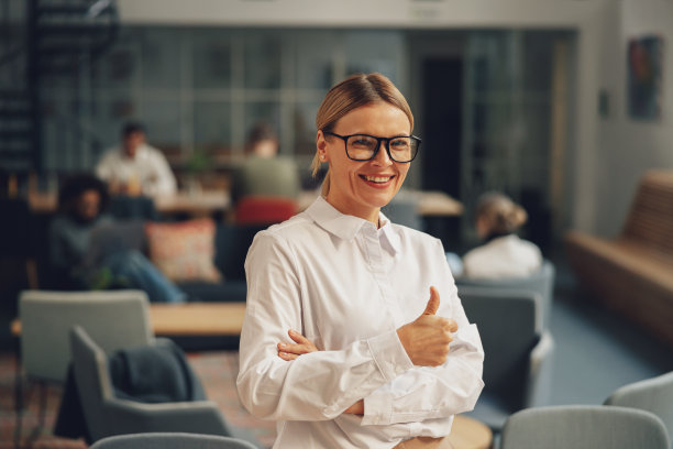中年女性办公室职员，戴眼镜，竖起大拇指站在同事的背景上图片下载