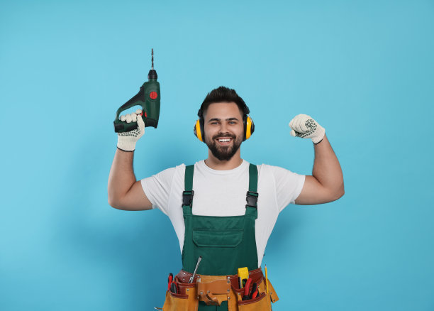 年轻的工人在制服与电钻浅蓝色背景图片下载