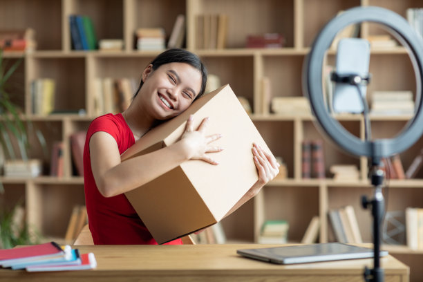 满意的少年日本女士抱着纸箱和拍摄视频博客在客厅内部图片下载