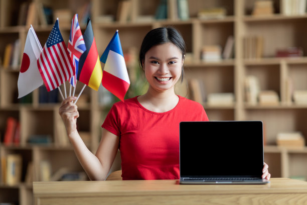 高兴的青春期韩国女学生拿着不同的旗帜在桌子与电脑空屏幕图片下载