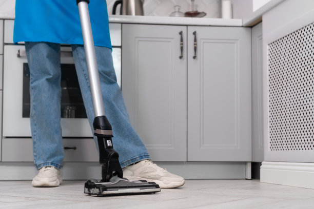 在现代厨房清洁时，一个女人手里拿着垂直真空吸尘器的特写。清洁公司的员工或家庭主妇打扫房子。图片下载