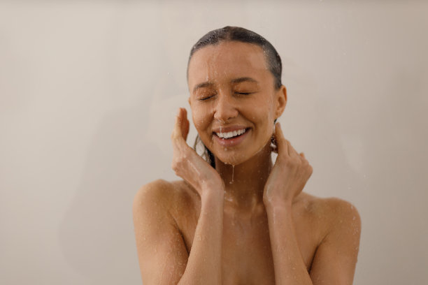 年轻女子在涓涓细流下愉快地淋浴。美丽的女孩在水的浪花下孤立的背景。湿了快乐的脸。图片下载