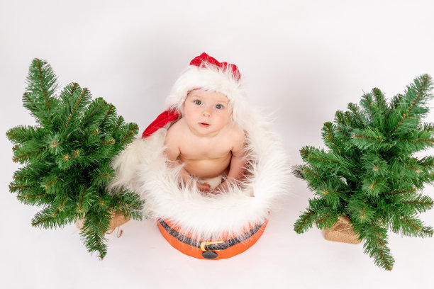 圣诞照片一个小女孩坐在圣诞树附近的篮子里，戴着圣诞帽，白色孤立的背景，俯视图，2021年新年快乐，文字空间图片下载