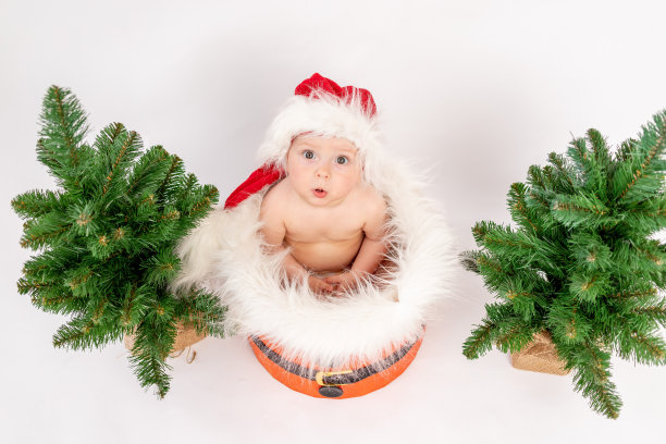 圣诞照片一个小女孩坐在圣诞树附近的篮子里，戴着圣诞帽，白色孤立的背景，俯视图，2021年新年快乐，文字空间图片下载