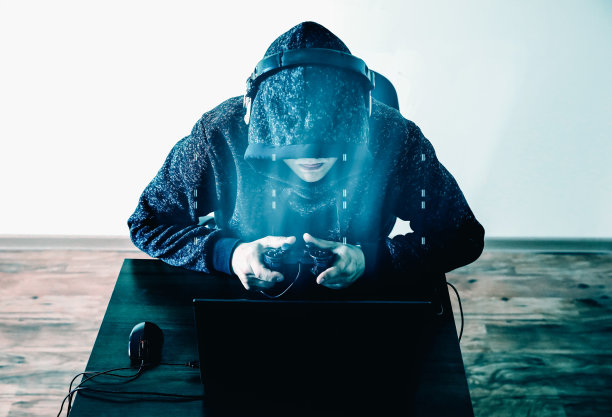 戴着耳机的游戏玩家：沉迷于电子游戏，穿帽衫的男人在电脑旁，手握游戏手柄图片下载