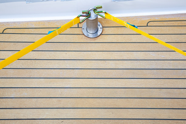 两条黄色的货物带被固定和拉紧在一个支柱上，支柱被螺栓固定在游艇的柚木甲板上。图片下载
