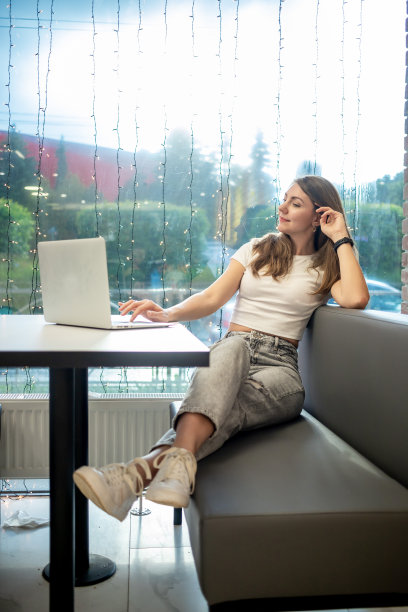 微笑的自由职业女孩在咖啡馆的笔记本电脑前工作，一个自由的年轻女人的工作日图片下载