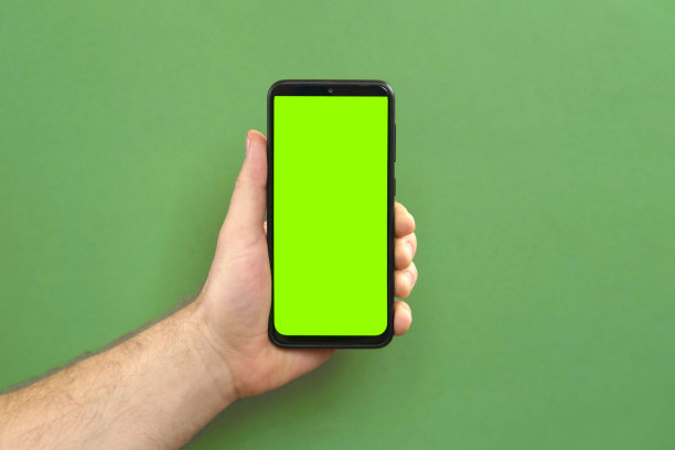 年轻人手里拿着手机。使用智能手机与空白绿色屏幕在绿色工作室背景。男性显示黑色手机与色度键显示。关闭了。模拟智能手机的广告，应用程序图片下载