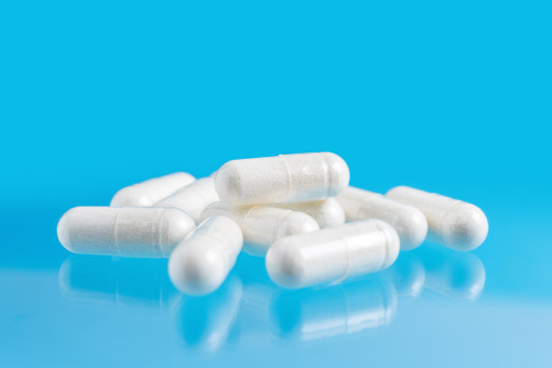 蓝色背景的白色治疗胶囊、维生素丸或治疗药物，医学和保健概念，特写视图图片下载