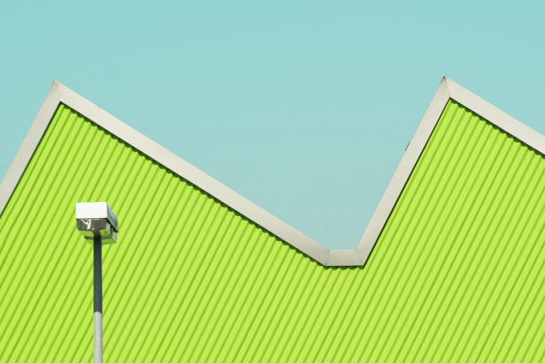 绿色波纹铁立面的侧面视图，锯齿状的屋顶和清晰的蓝色天空前的路灯图片下载