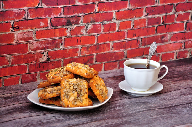 木桌上有一个盘子，里面放着一堆松饼饼干和花生，还有一杯热茶。图片下载