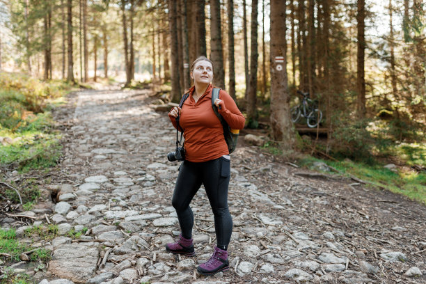 独自旅行的女子在秋天森林的小径上徒步旅行。全身照片。快乐的红头发的人在积极徒步旅行的衣服上走在自然背景。旅行和积极的生活方式概念。图片下载