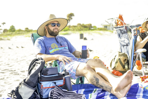 40多岁的快乐男人在田园诗般的海滩度假，坐在沙滩椅上，戴着遮阳帽图片下载