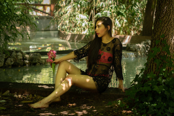 委内瑞拉棕发女孩粉红色比基尼和黑色渔网帕雷奥。坐着。半裸的女孩在公园的树林里。图片下载