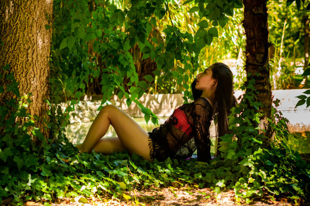 委内瑞拉棕发女孩粉红色比基尼和黑色渔网帕雷奥。坐着。半裸的女孩在公园的树林里。图片下载