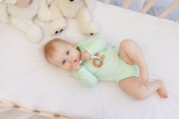 可爱的婴儿在婴儿床和牙齿在卧室在绿色紧身衣图片下载