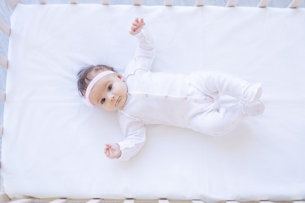 女婴在白色棉床的床上微笑，入睡或早上醒来，可爱的新生儿宝宝在家里的婴儿床上特写图片下载