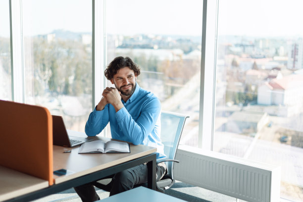 微笑的商人坐在办公桌在办公室的肖像图片下载