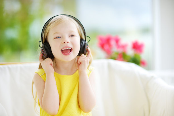 可爱的女孩戴着巨大的无线耳机。漂亮的孩子在听音乐。女生在家里听儿歌玩得很开心。图片下载