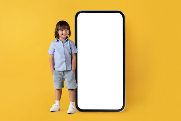 可爱快乐的小男孩对着镜头微笑，在大空白智能手机附近摆姿势，手放在口袋里，空无一物图片下载